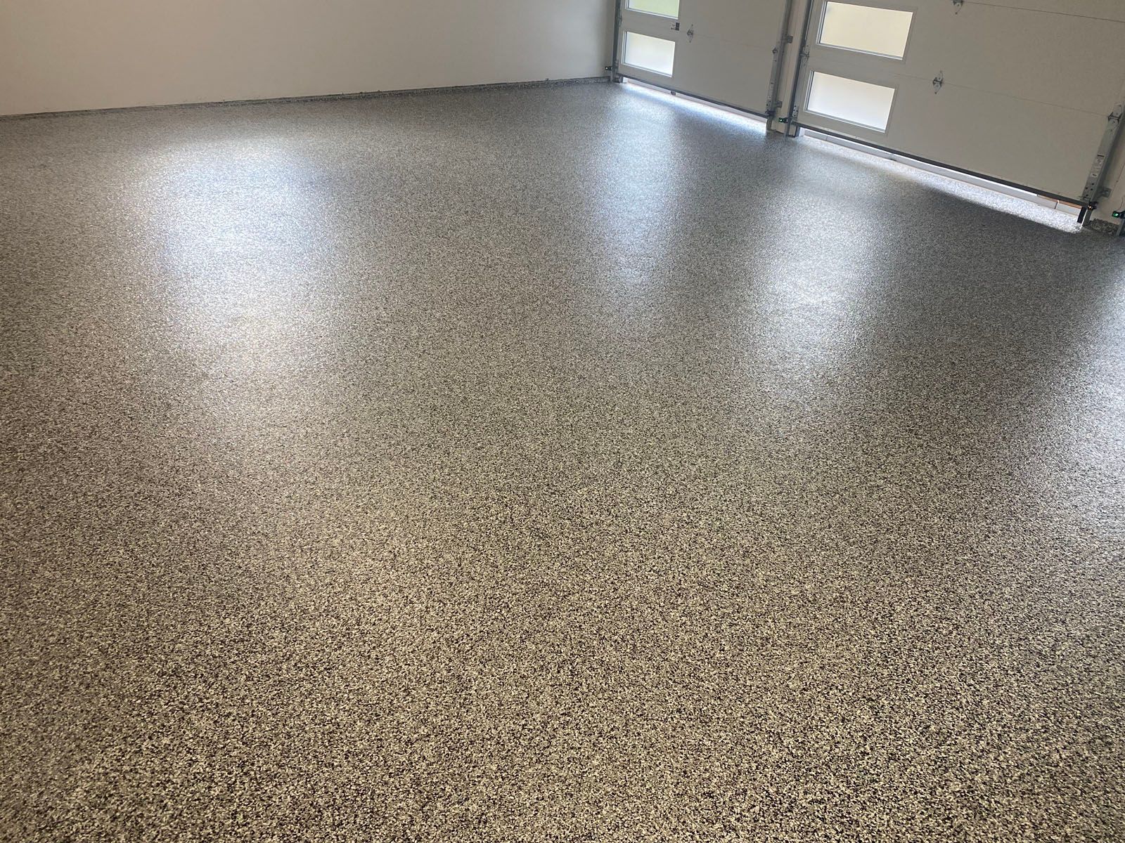A garage floor with a grey, black, and white speckled epoxy flake coating finish.