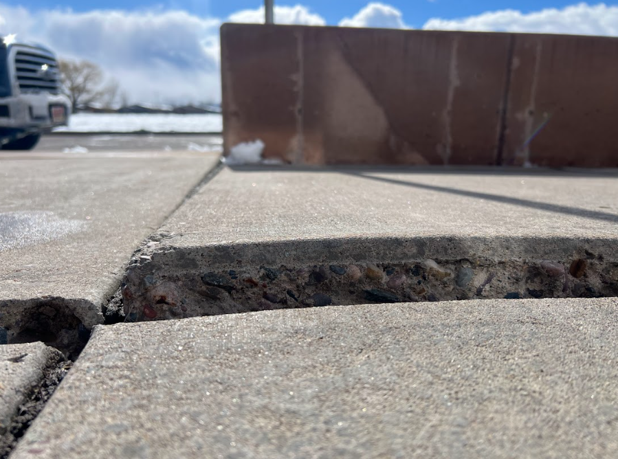 A sidewalk slab is unevenly raised, creating a significant tripping hazard with a wide gap between concrete sections.