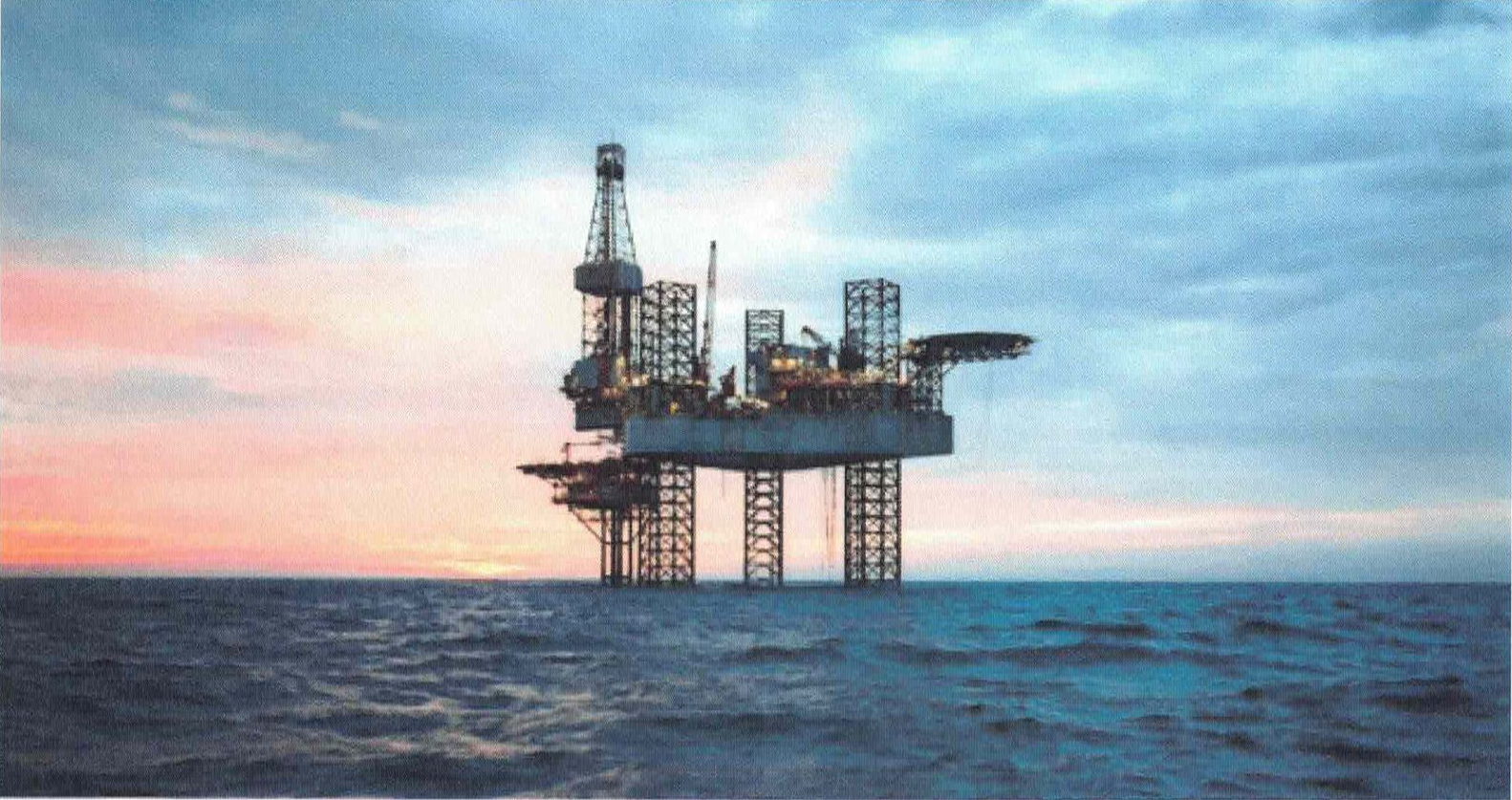 Offshore oil rig at dusk on a calm sea, with orange and blue sky.