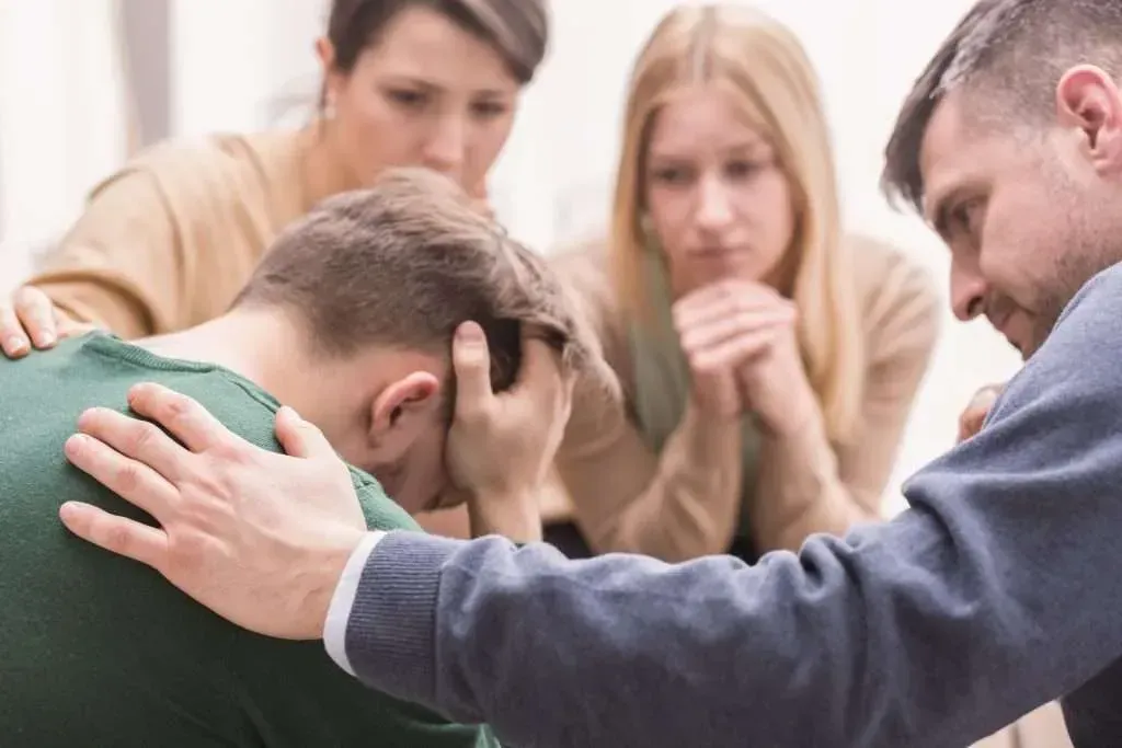 A group of people are sitting around a man with his head in his hands.