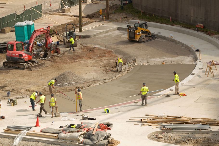 Construction workers paving a curved road with heavy machinery and traffic cones