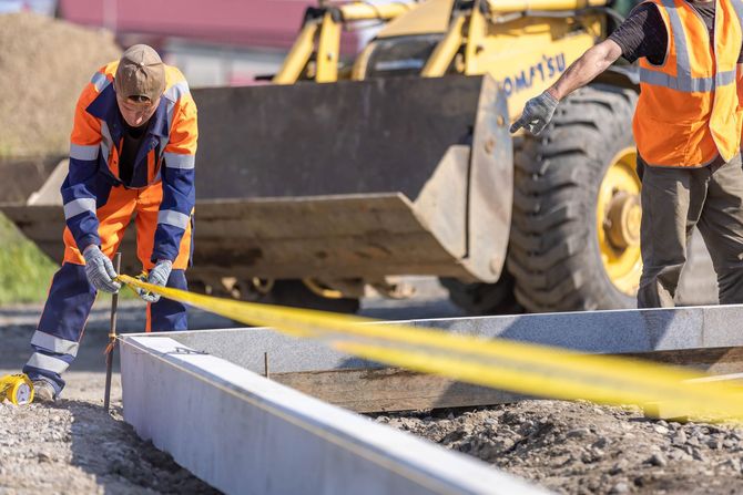 Road crew in orange safety gear pouring concrete beside a yellow loader on a construction site