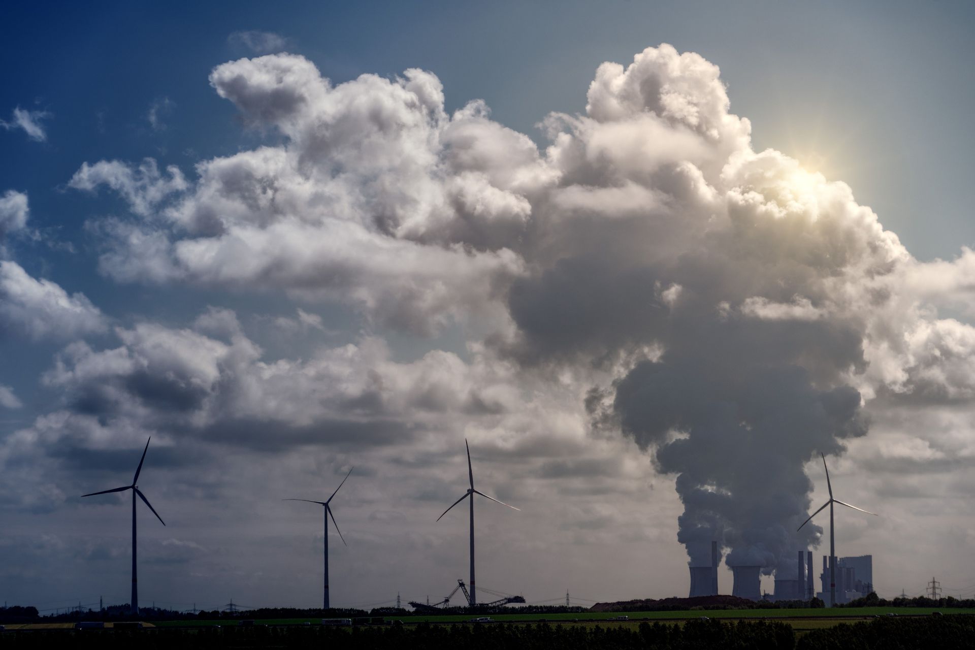 Natural Gas Plant with tall smokestacks and metal structures emitting steam against a blue sky with clouds.