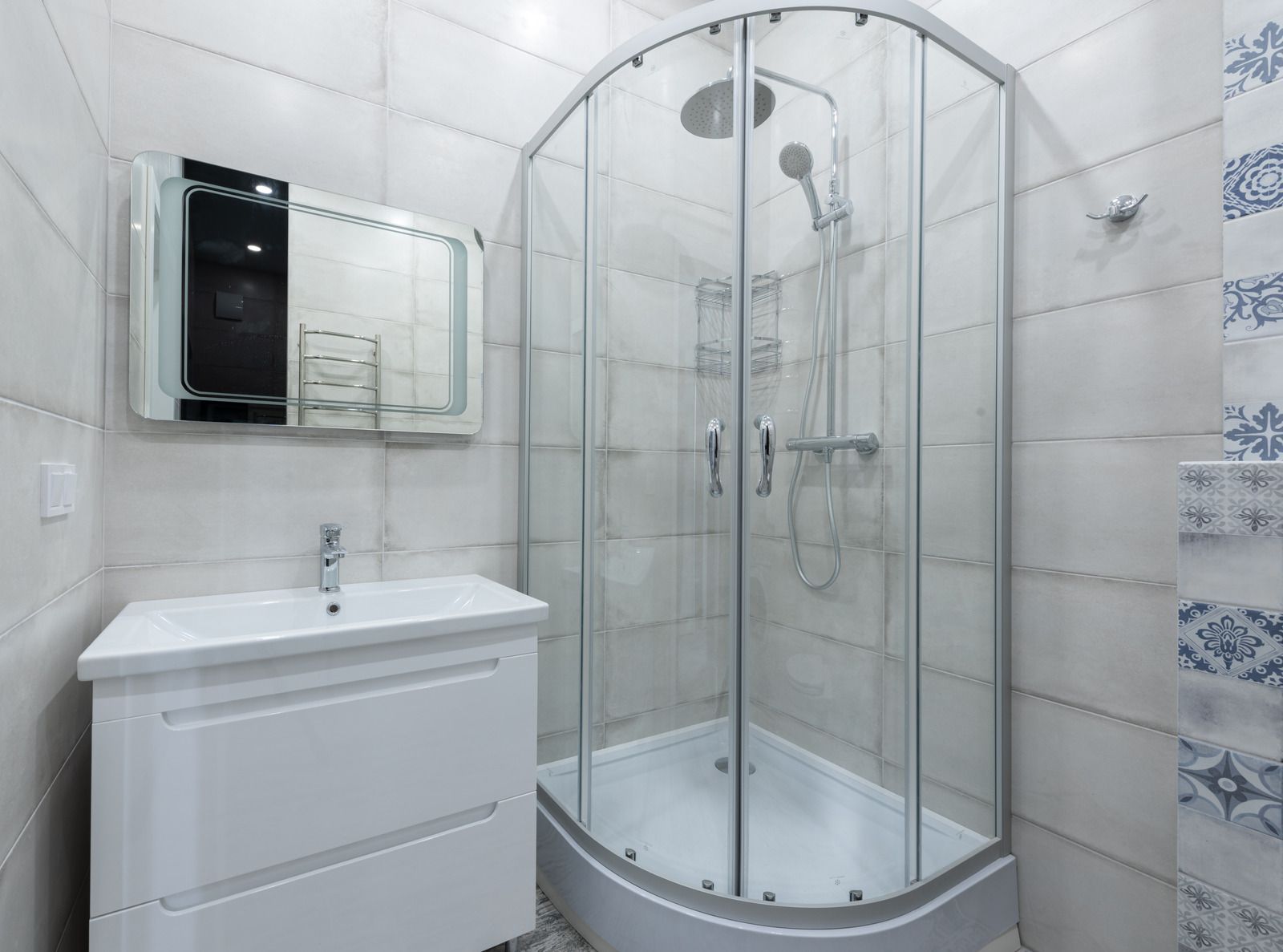 Walk-in shower with marble-look tile, chrome fixtures, and white shower pan