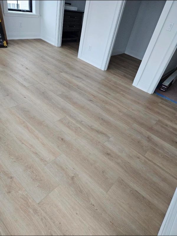 Light wood flooring in a mostly empty white room with open doorways and a hallway.