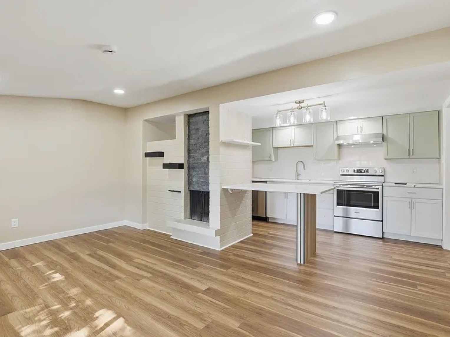 Empty modern kitchen and living area with white cabinets, stainless appliances, and wood floors