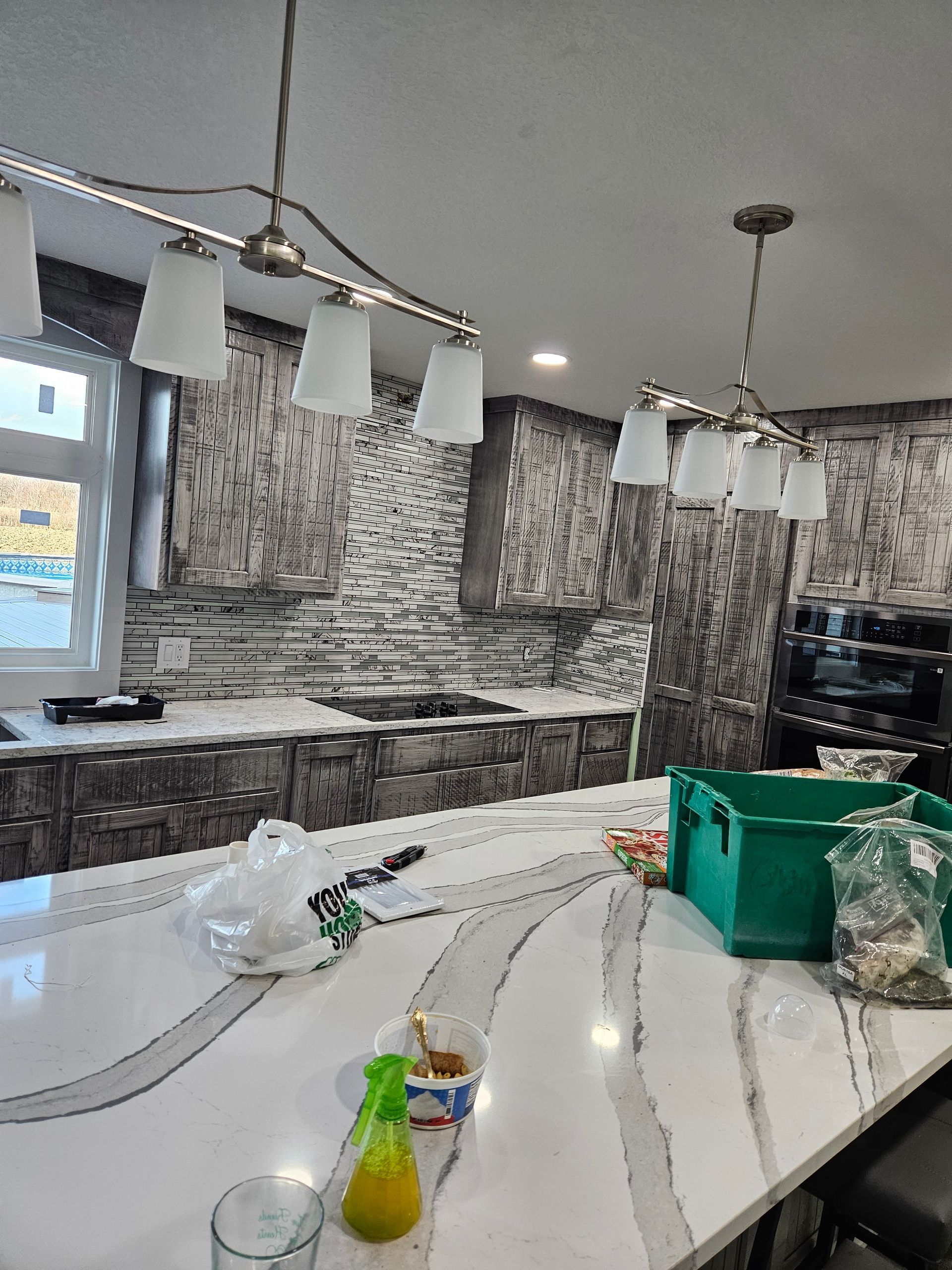 Modern kitchen with marble island, pendant lights, and gray mosaic backsplash, viewed from the counter