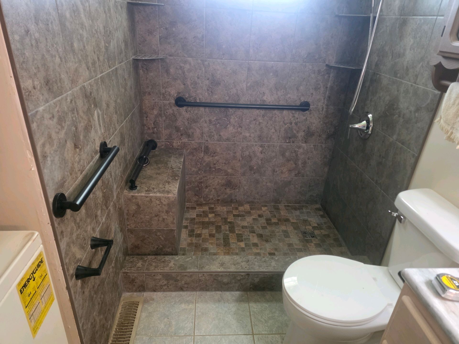 Accessible bathroom with tiled walk-in shower, grab bars, and a toilet in the foreground.