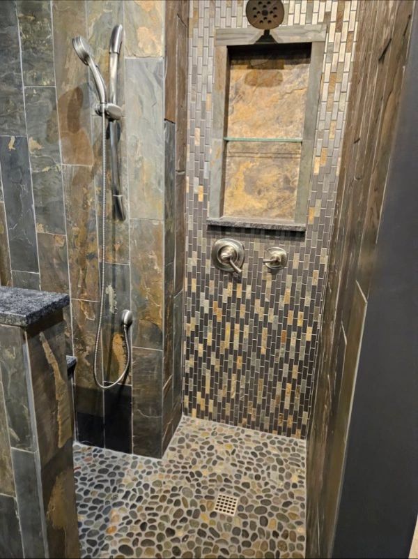 Modern tiled shower with stone floor, rainfall showerhead, and recessed shelf niche