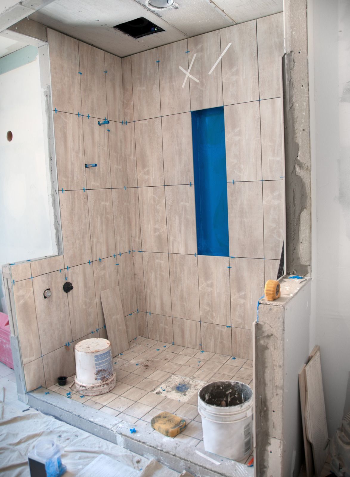 Partially tiled shower under renovation with blue waterproofing, buckets, and tools on the floor