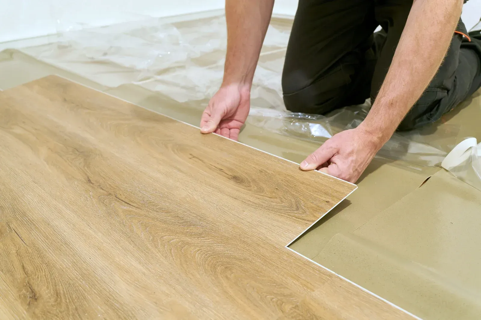 Person installing a wood-look floor plank, aligning it with existing flooring indoors