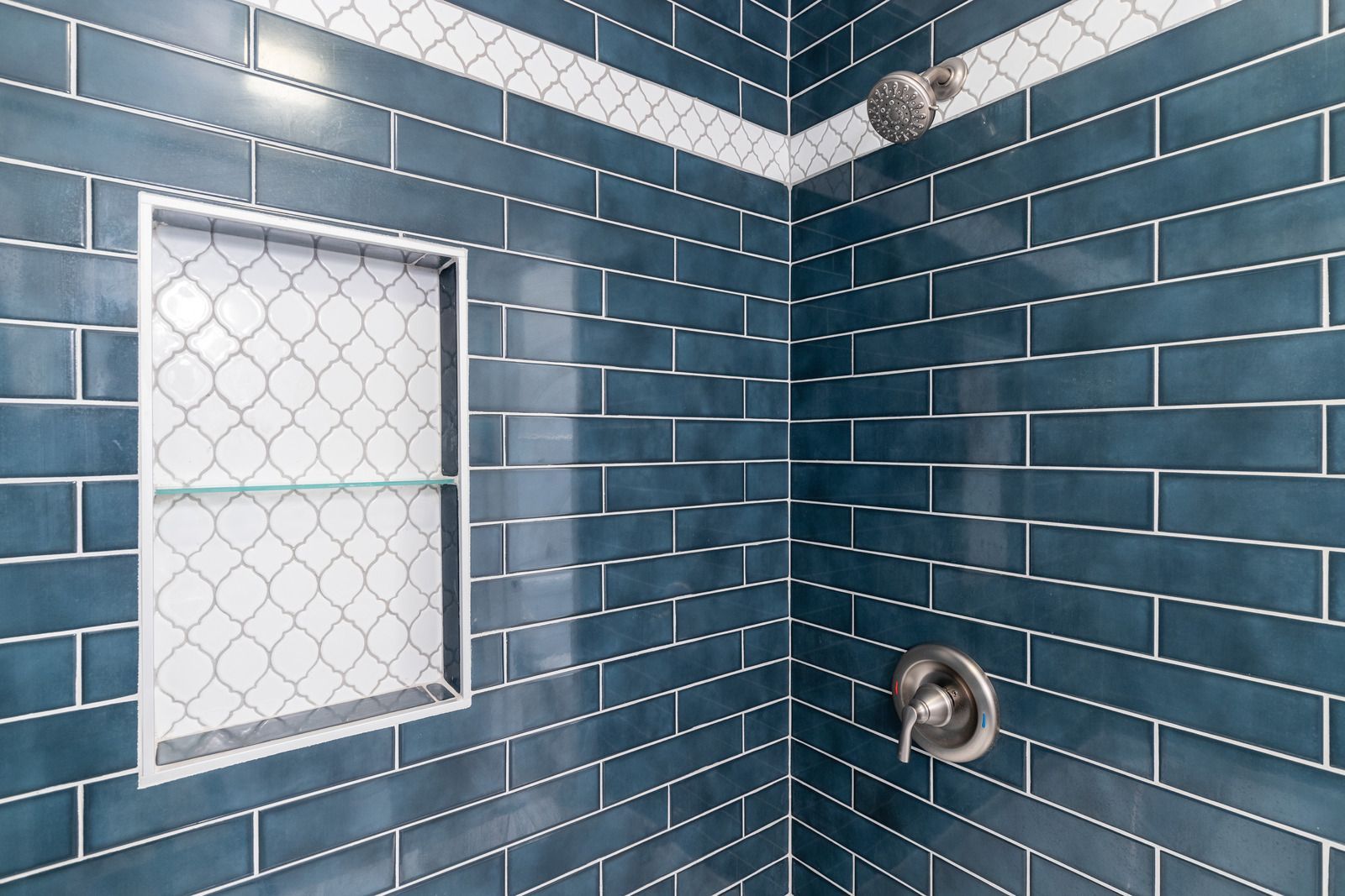 White tiled bathroom with built-in corner shelves and bright sunlight on the floor.