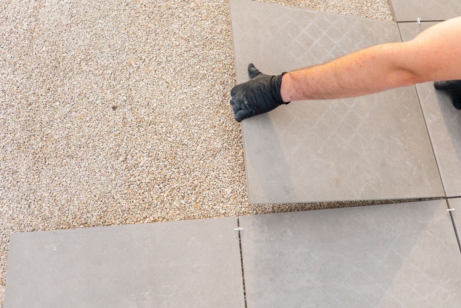 Gloved hand wiping dust from a tiled floor near a wall