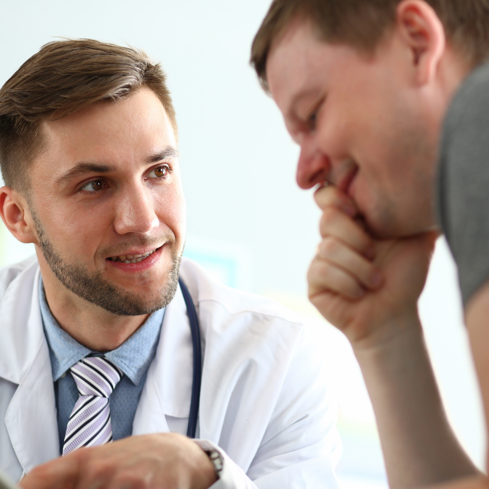 Doctor speaking with a patient in a clinic, both leaning in during a consultation.