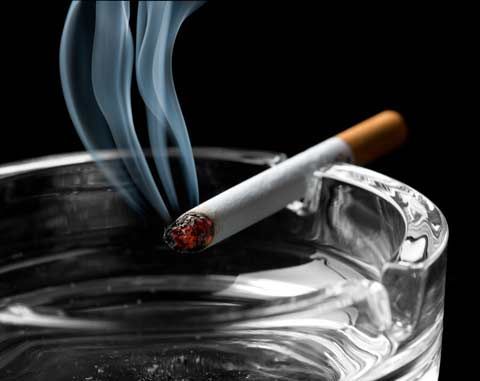 Lit cigarette in an ashtray with wisps of smoke against a black background