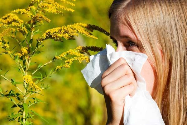 Woman wiping her nose with a tissue near yellow wildflowers in a sunny field