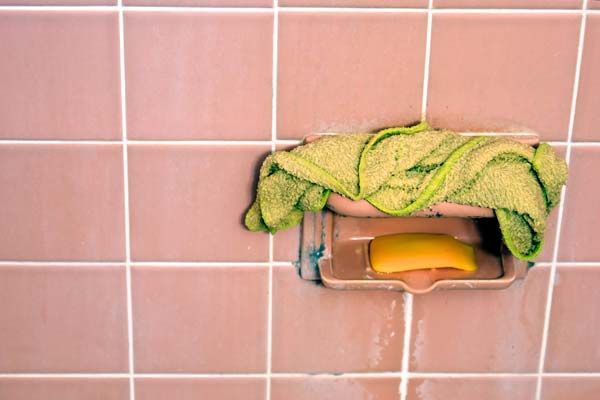 Soap and green cloth on a small wall-mounted shelf against pink tiled wall
