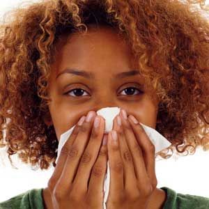 Person holding a tissue to their nose, appearing to blow it, with curly hair and a green shirt.