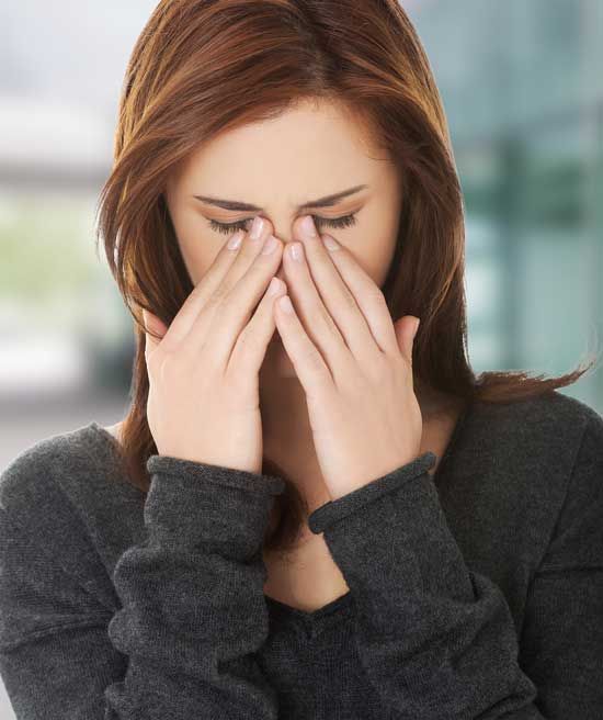 Woman in a dark sweater rubbing her eyes, looking tired or stressed.