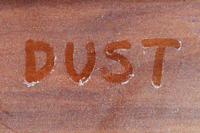 The word “DUST” written in orange on a brown sandy surface.
