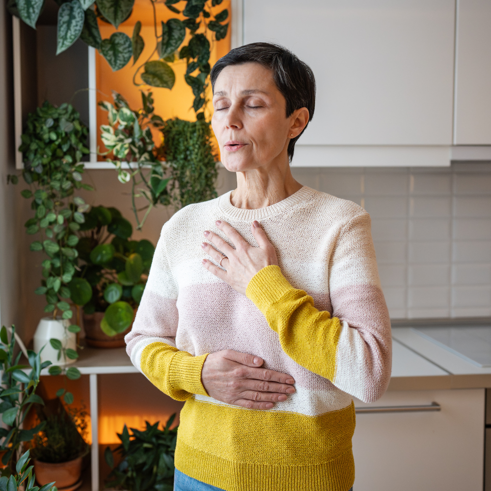 Person in a yellow and white sweater holding chest and stomach, standing in a kitchen.