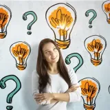 Woman smiling with arms crossed, surrounded by lightbulbs and question marks on a white background