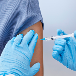 Gloved hands preparing a syringe injection into an arm in a clinical setting