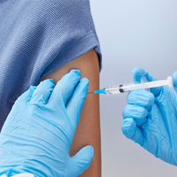 Gloved hands preparing a syringe injection into an arm in a clinical setting