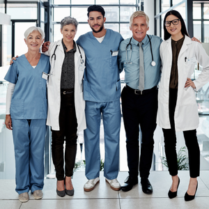 Group of five medical professionals in scrubs and lab coats standing together in a bright hospital hallway