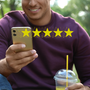 Man smiling while using a gold phone outdoors beside a cold drink on a table