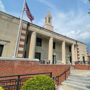 Historic building with columns, brick wall, steps, and an American flag under a blue sky