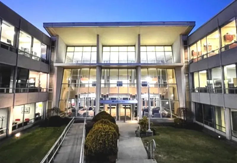 Modern office building courtyard at dusk with illuminated glass windows and central walkway