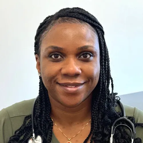 Smiling medical professional in olive scrubs with a stethoscope against a light background