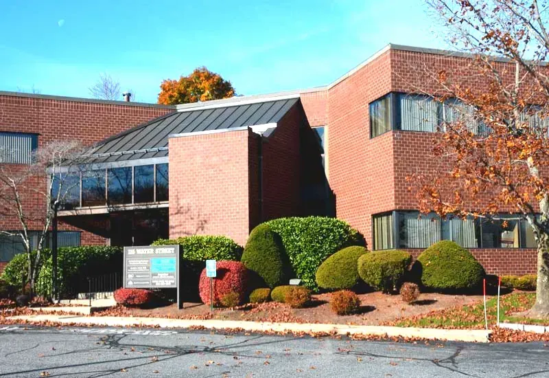 Brick office building with large windows, glass entrance, and landscaped shrubs in front