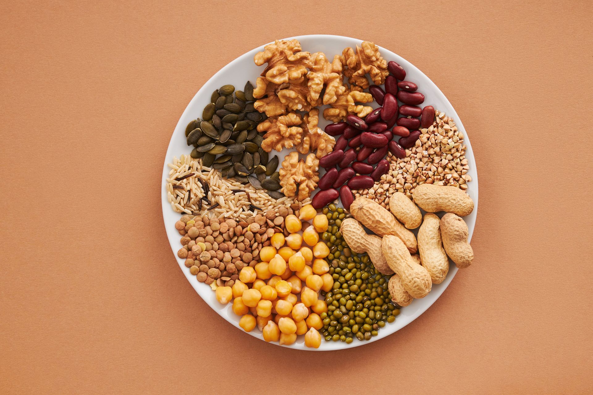 White plate of assorted nuts and dried fruits on a tan background