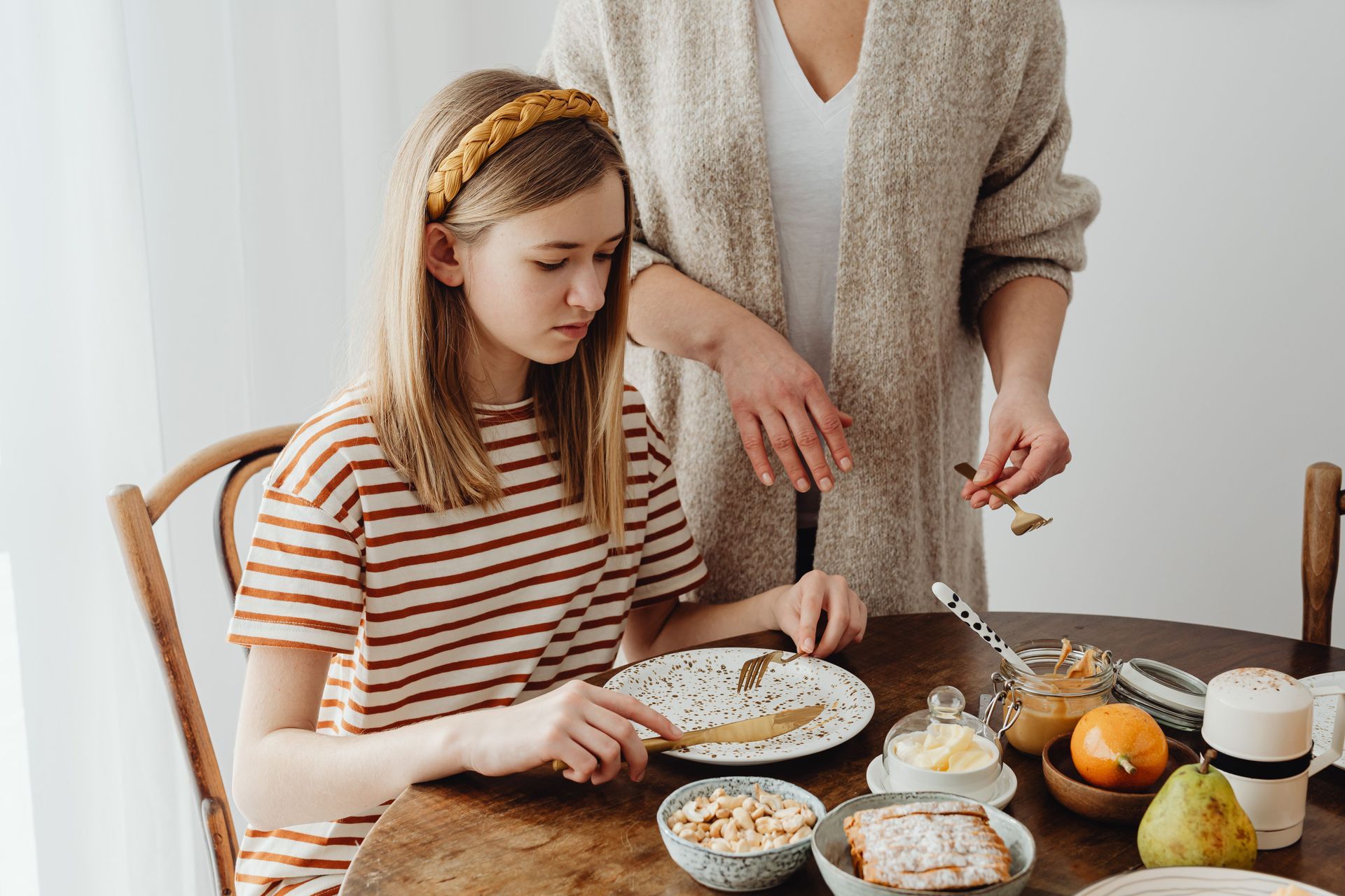 Person and child setting a breakfast table with cereal, fruit, and drinks in a bright kitchen