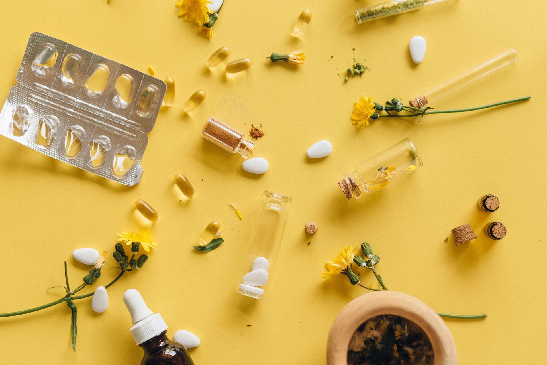 Assorted yellow flowers, herbs, and supplement capsules on a yellow background