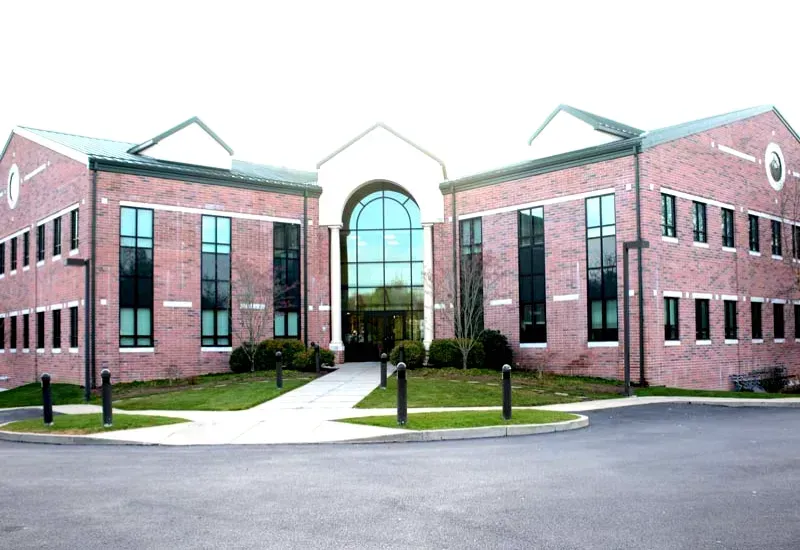 Red brick office building with a central glass entrance and walkway, seen from the front.