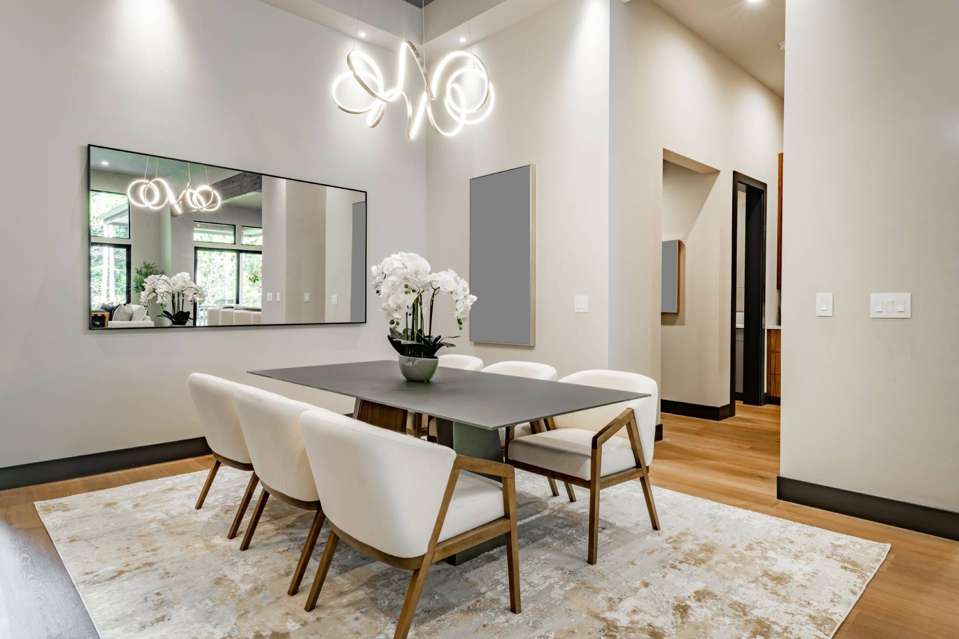 Dining room with a gray table, white chairs, rug, and a large mirror.
