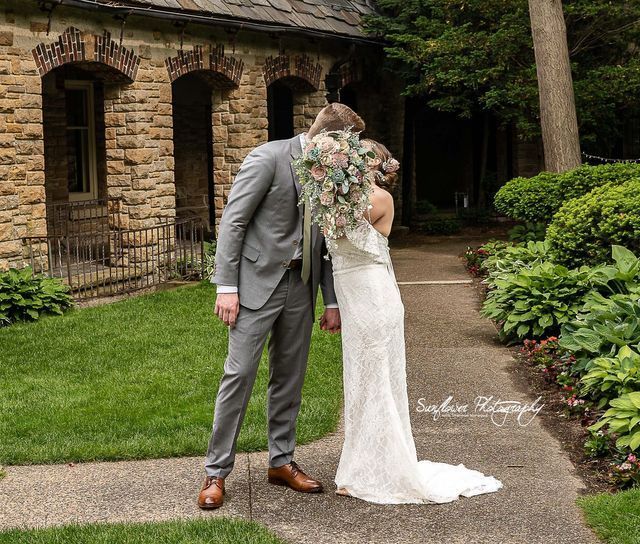 A bride and groom are kissing in front of a stone building.