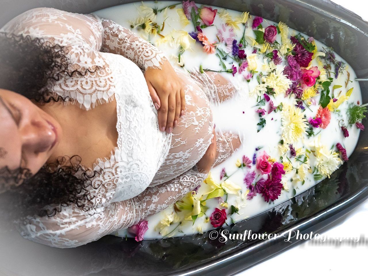 A pregnant woman is laying in a bathtub filled with milk and flowers.