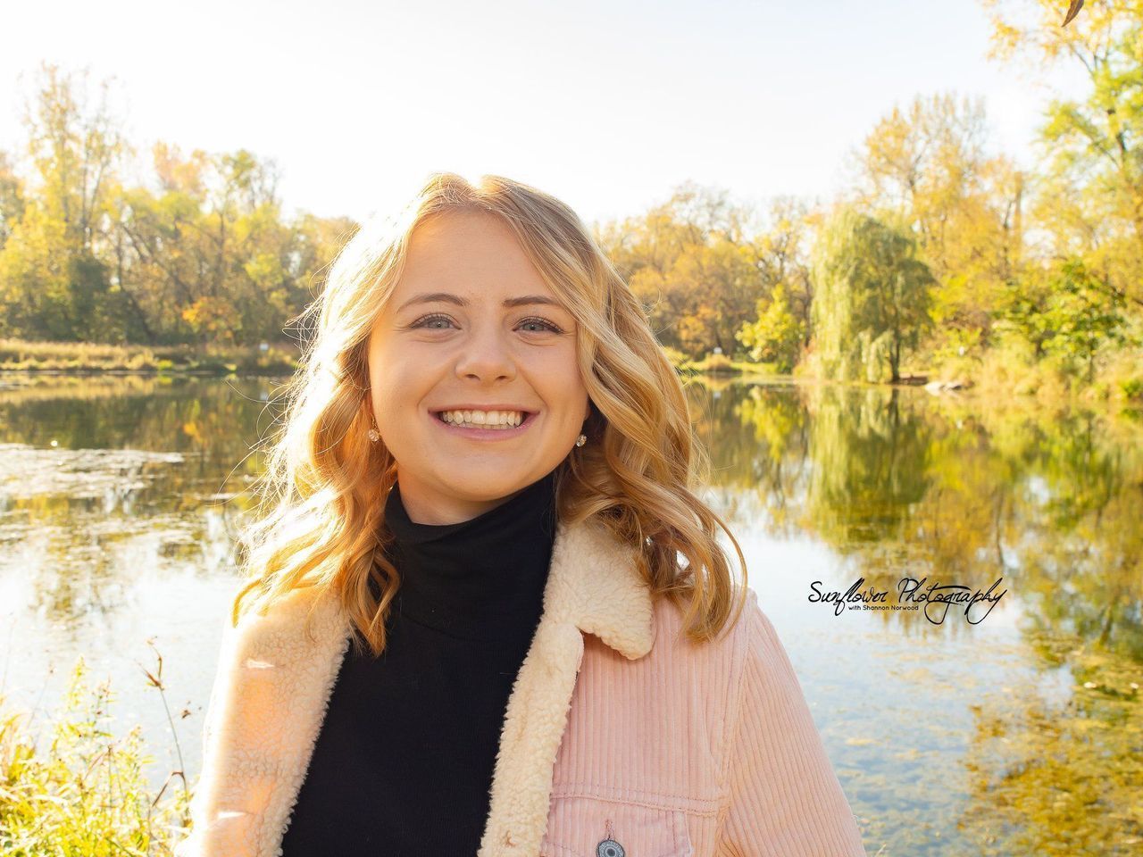 A young woman is smiling in front of a lake.