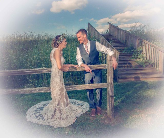 A bride and groom are standing next to a wooden fence.