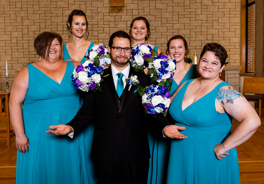A bride and groom are posing for a picture with their bridesmaids in blue dresses.
