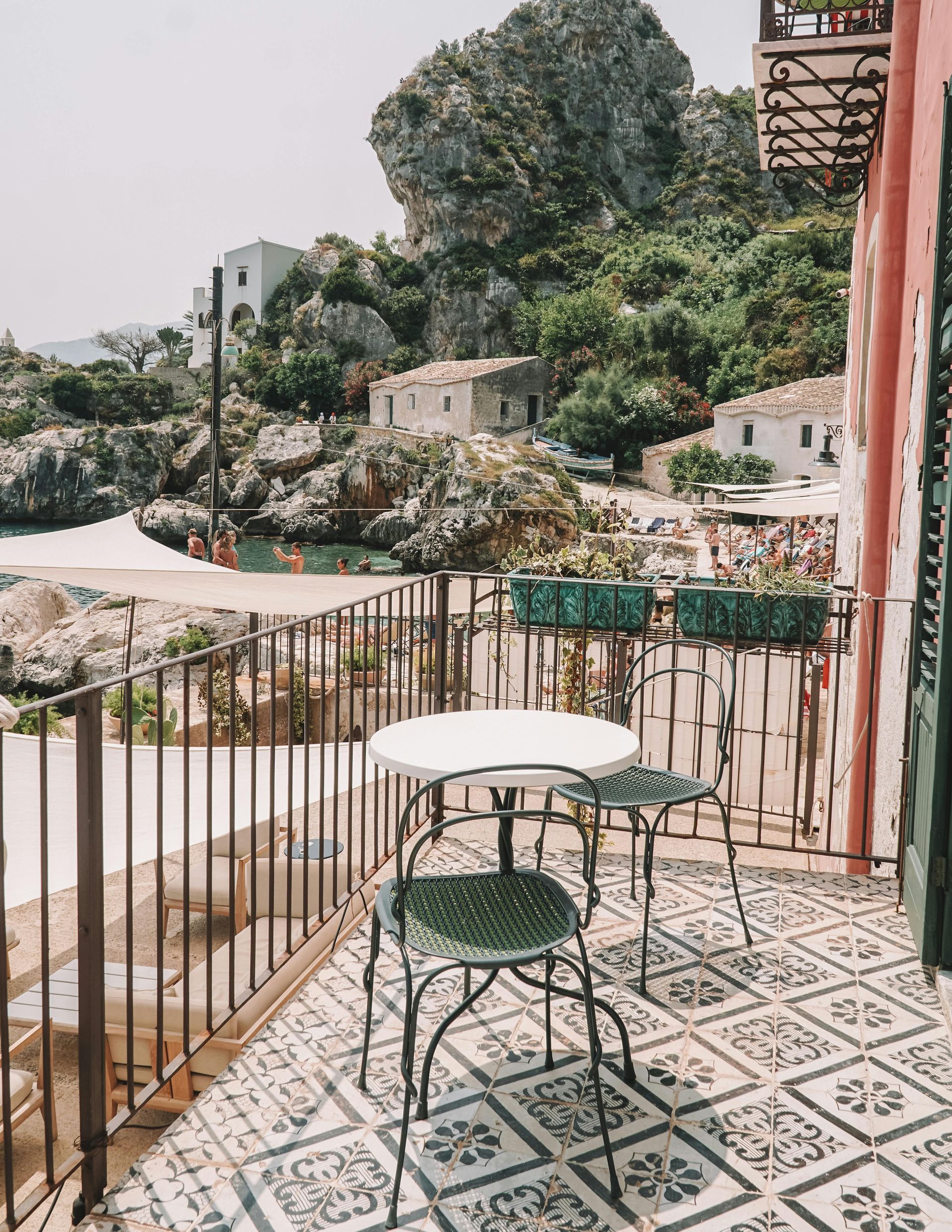 Balcone con vista su una baia con tavolo e sedie, edifici e una grande formazione rocciosa.
