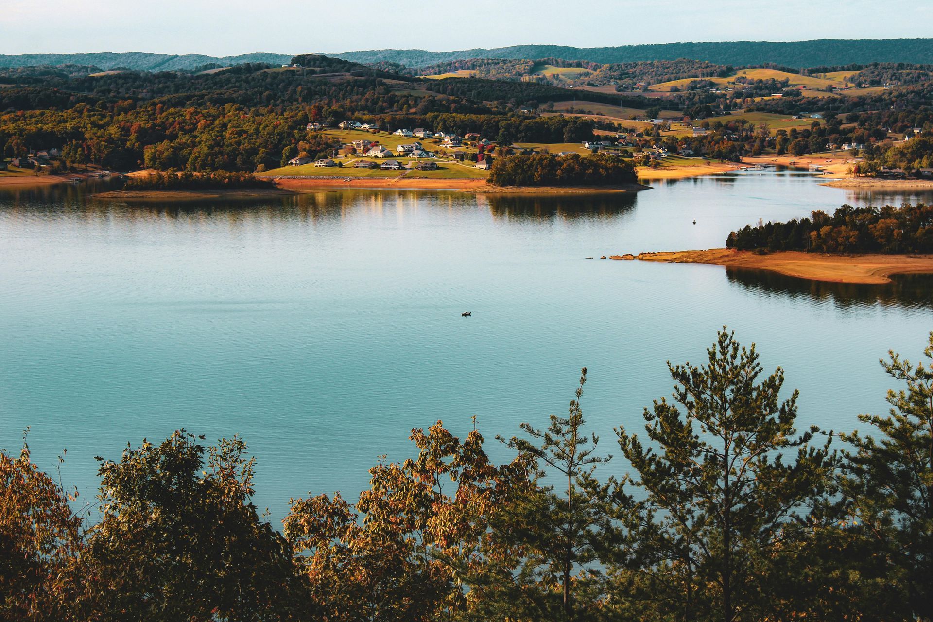 Uno scenario sereno su un lago con alberi, una cittadina sulla riva e dolci colline sullo sfondo.