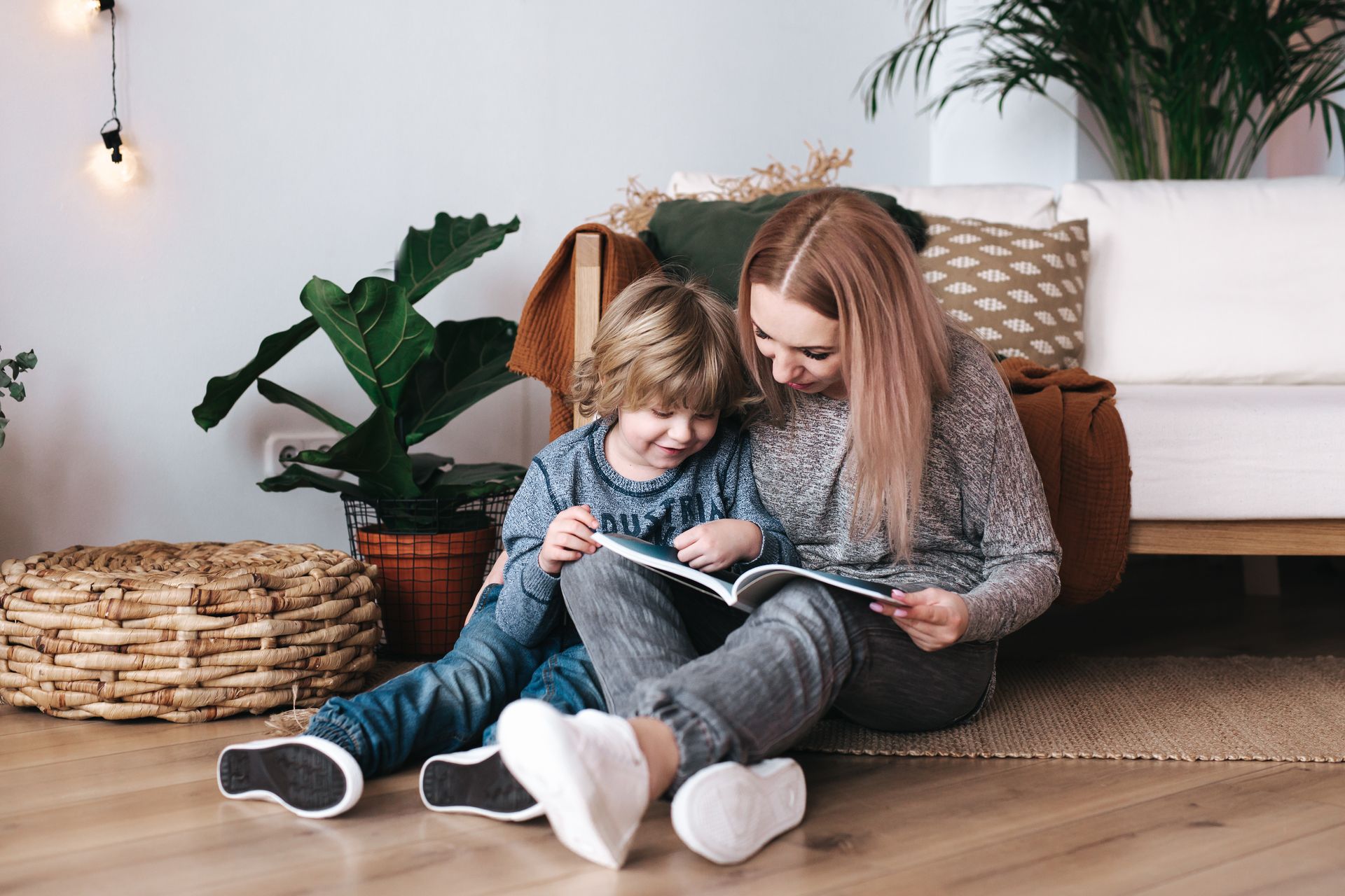 A woman and a child are sitting on the floor reading a book.