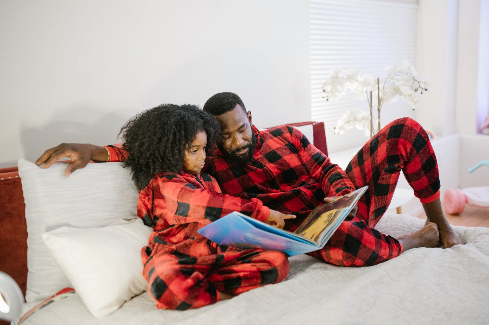 A man and a woman are sitting on a bed reading a book.