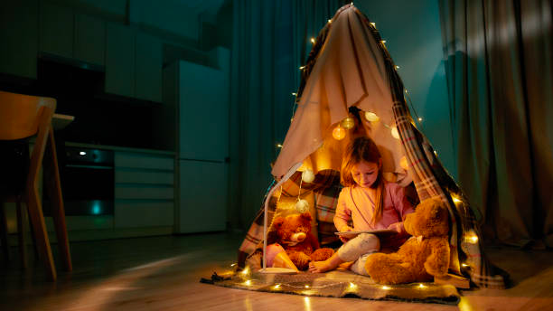 A little girl is sitting in a teepee reading a book.