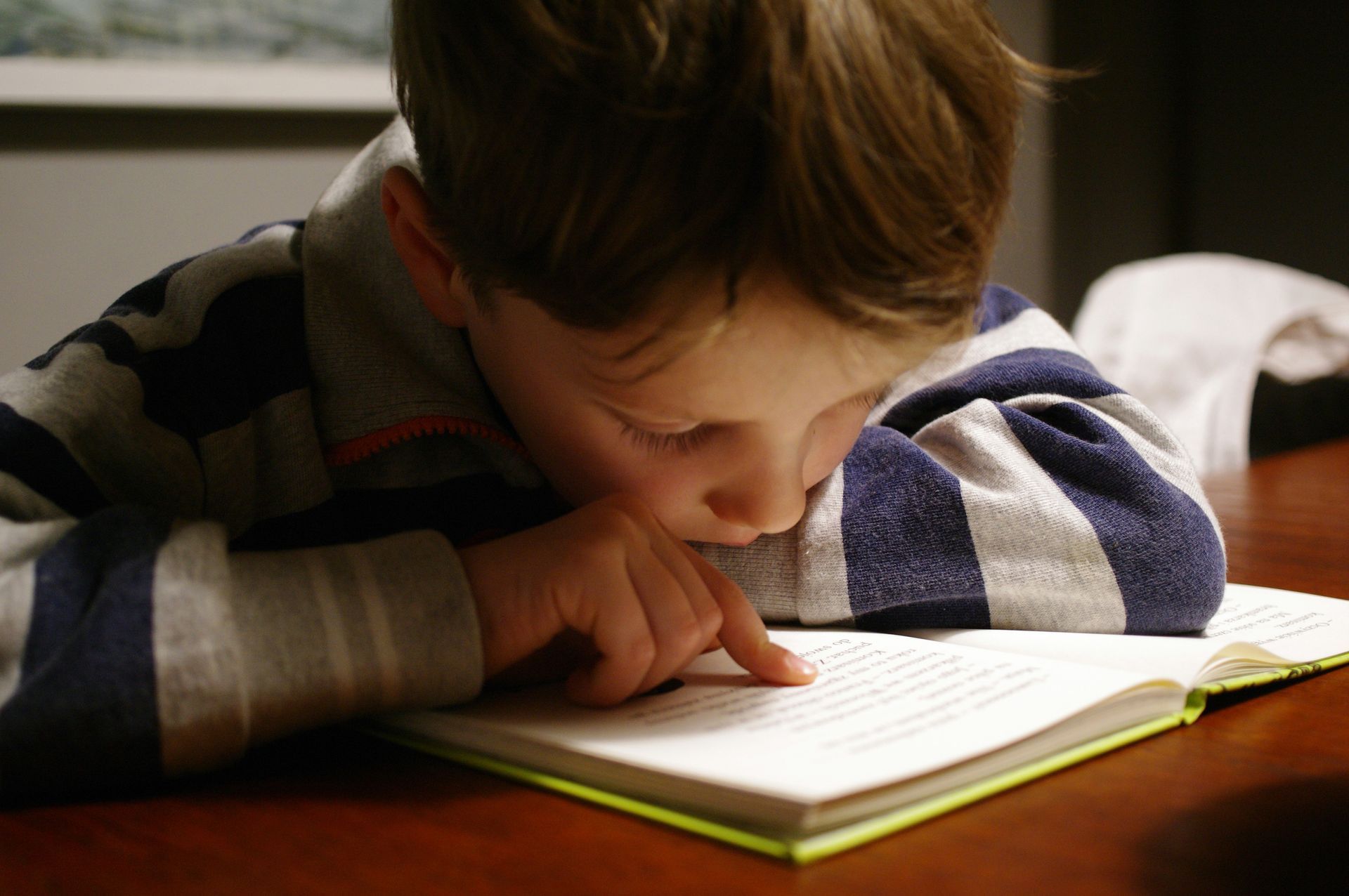 A young boy is laying on a table reading a book.